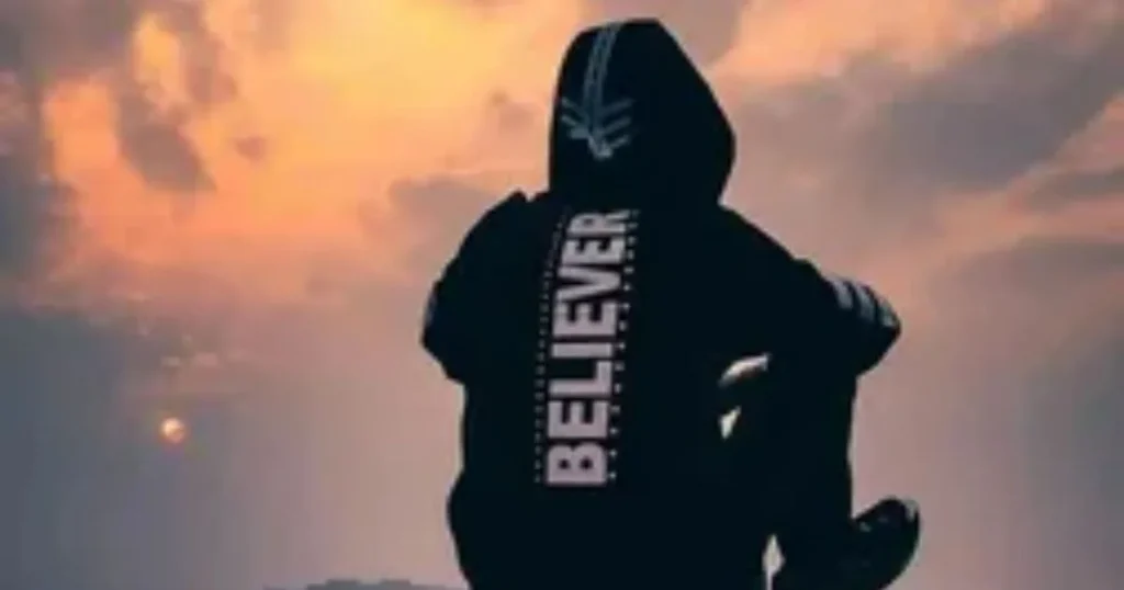Attitude boy sitting alone in a black Believer hoodie, looking at an orange sunset sky