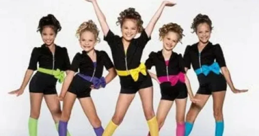 Five young dancers posing in black outfits with colorful bows and matching socks