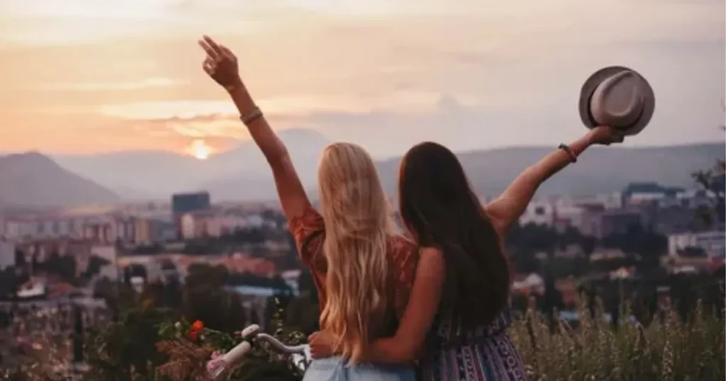 Two best friends standing together with their arms raised while watching a beautiful sunset over the city.
